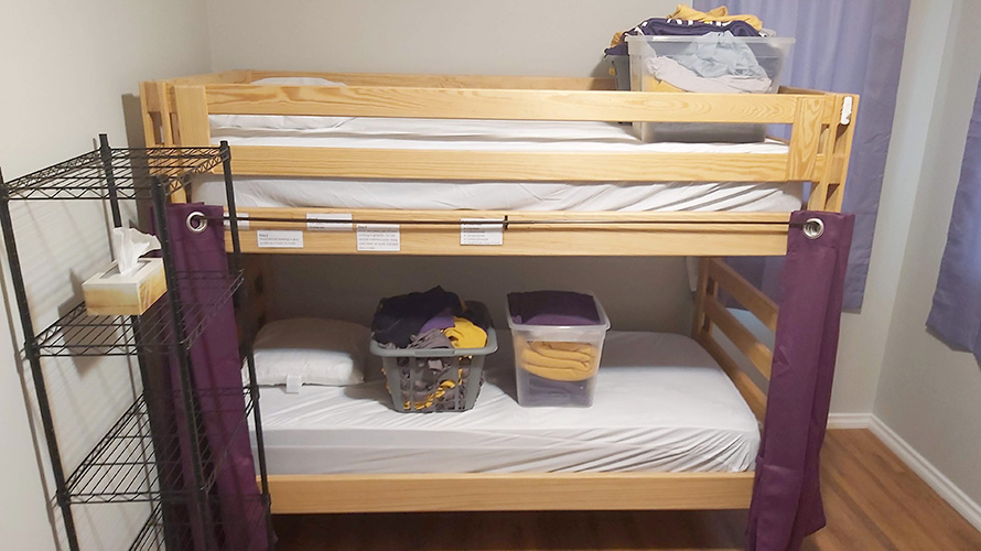 A set of bunk beds with bins of Laurier themed clothing on top and a wire shelving unit.