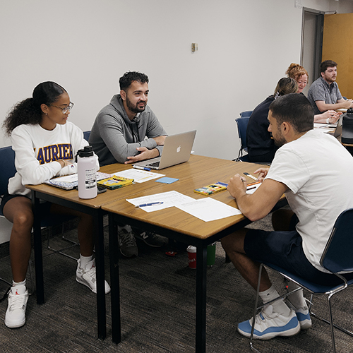 Three students sitting at desks in a classroom working on an activity together