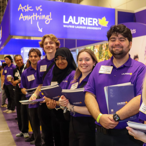 student ambassadors lined up in front of Laurier's OUF booth smiling