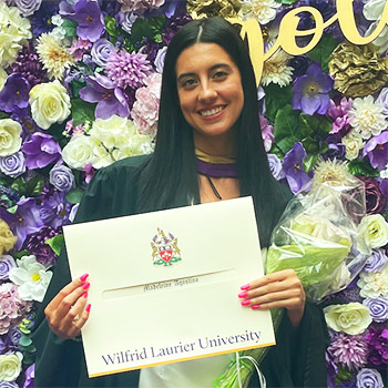 student with black hair and diploma in front of flower wall